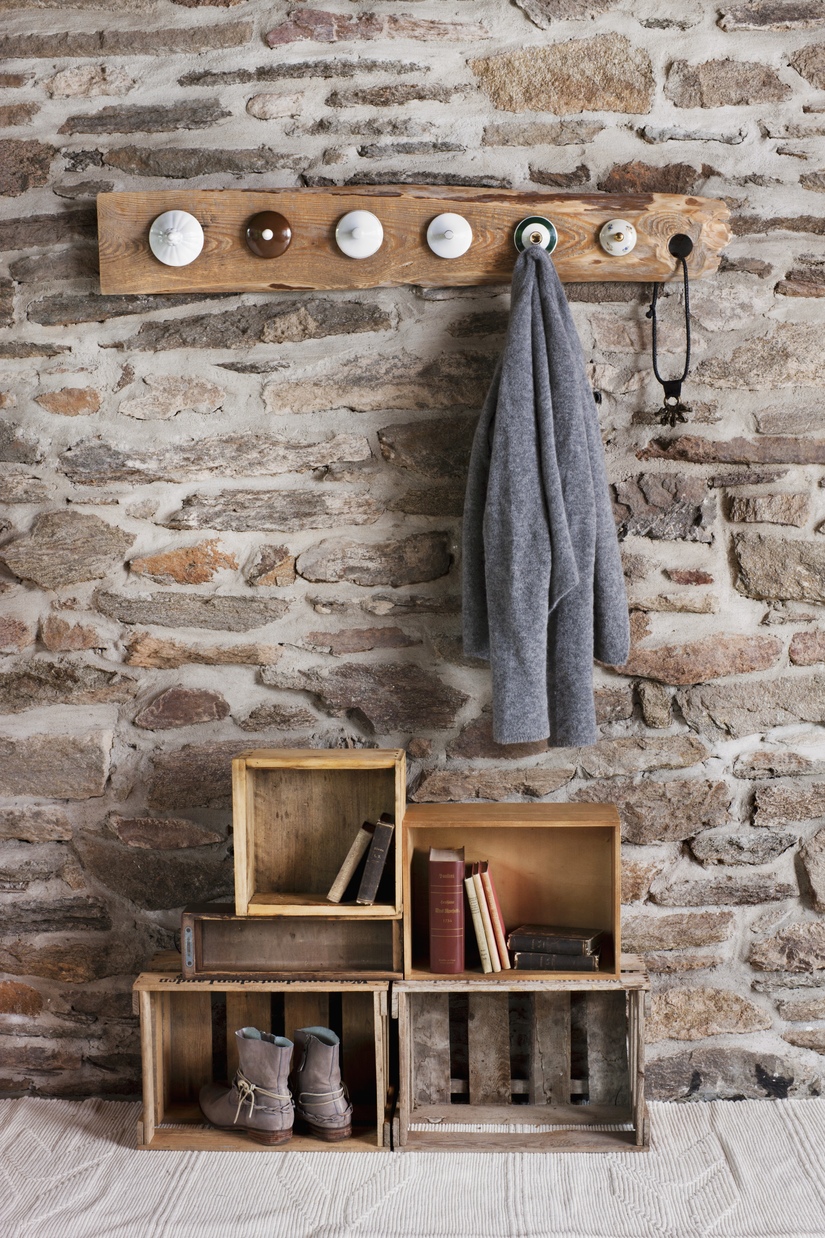 Vestiaire bricolage rustique dans la chambre avec mur de pierre; piquets en vieux couvercles en porcelaine et vieilles caisses en bois sur le sol comme rangement